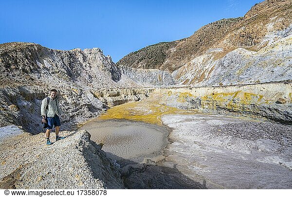 Young man at the crater rim  crater with yellow discoloured sulphur stones  volcano caldera with pumice fields  Alexandros crater  Nisyros  Dodecanese  Greece  Europe