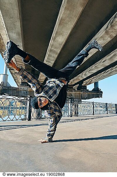 Young man break dancer dancing on urban background performing acrobatic stunts. Street artist breakdancing outdoors