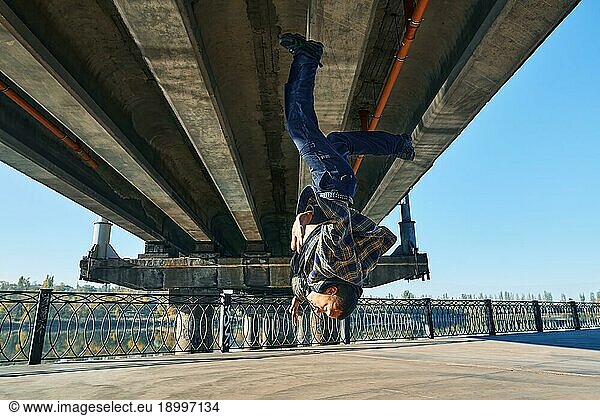 Young man break dancer doing somersault acrobatic stunts dancing on urban background. Street artist breakdancing outdoors