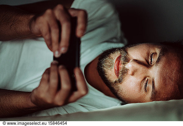 Young man cannot sleep and is watching something on his phone