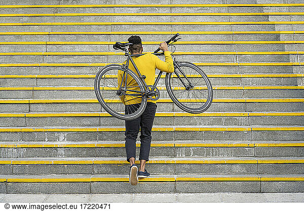 Young man carrying bicycle while climbing on staircase