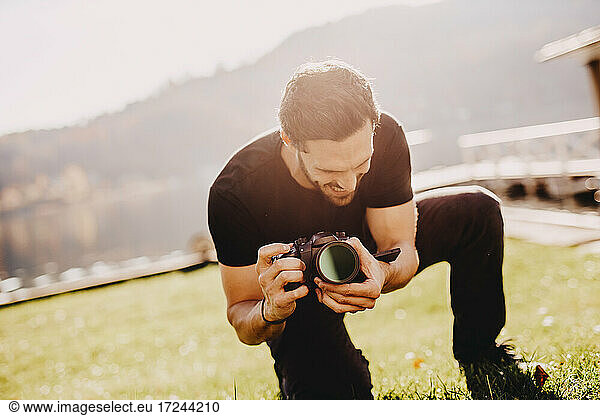 Young man crouching while using camera on lawn