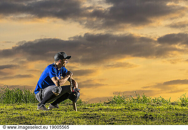 Young man crouching with baseball bat at dusk