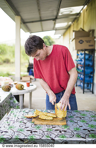 Young man cutting fresh  organic pineapple on wood cutting board.