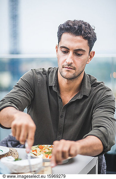 Young man cutting mozzarella at building terrace during party