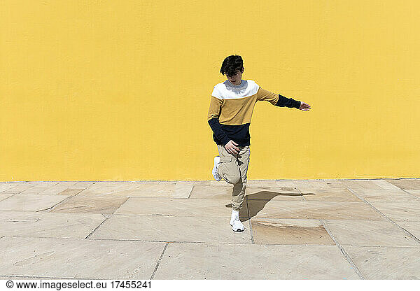 Young man dancing in front of yellow wall