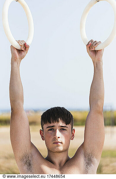 Young man doing calisthenics exercises on rings outdoors.