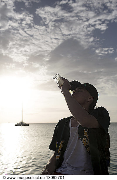 Young man drinking beer by sea