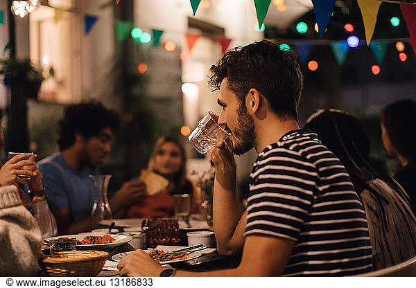 Young man drinking water while having dinner with friends during garden party