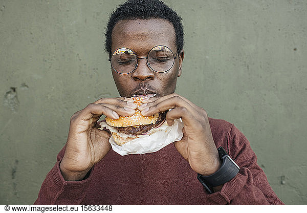 Young man eating cheeseburger  with eyes closed