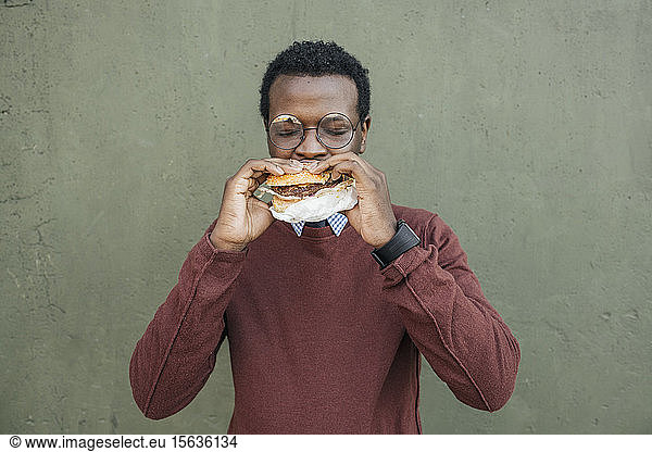 Young man eating cheeseburger  with eyes closed