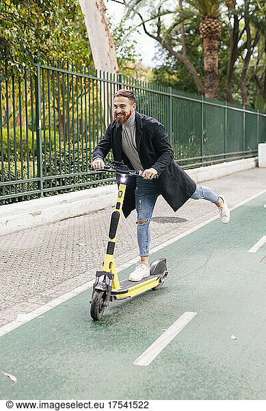 Young man enjoying electric push scooter ride on bicycle lane