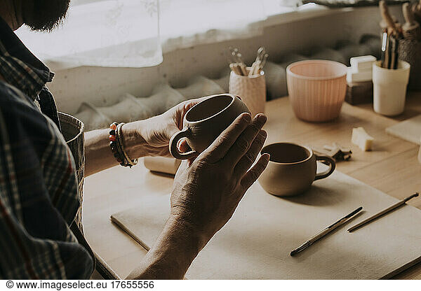 Young man examining earthen cup in workshop