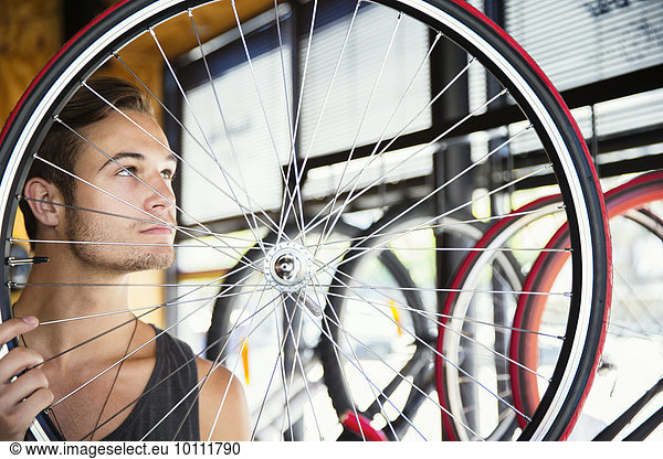 Young man examining spokes on wheel in bicycle shop