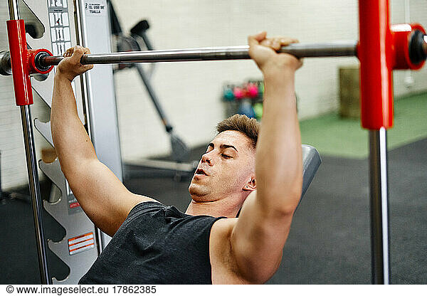 Young Man Exercising In Gym With Bench Press