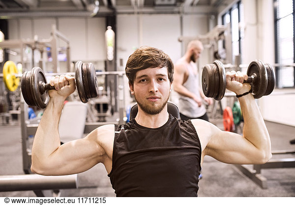 Young man exercising with dumbbells in gym