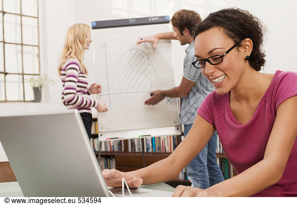 Young man explaining woman chart in background focus on woman using laptop smiling