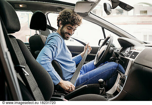 Young man fastening seat belt sitting in car