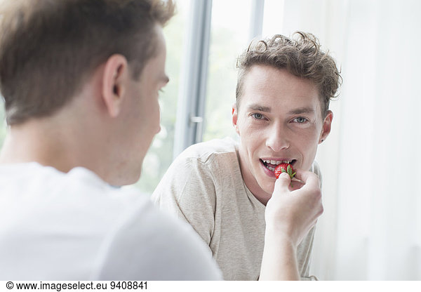 Young man feeding strawberry to another man  smiling
