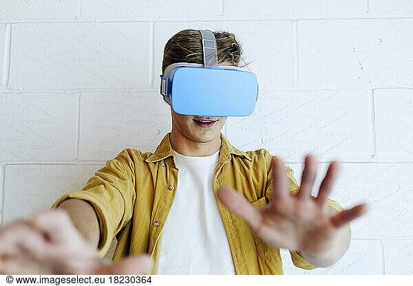 Young man gesturing wearing virtual reality headset in front of white wall