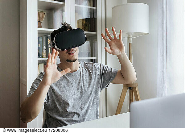 Young man gesturing while wearing Virtual reality headset at home office