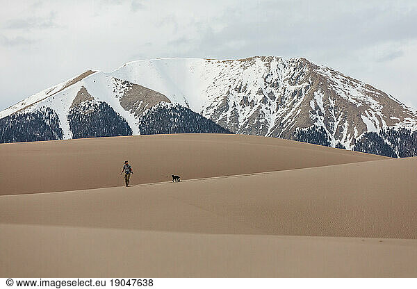 young man hikes with dog in the great sand dunes of colorado