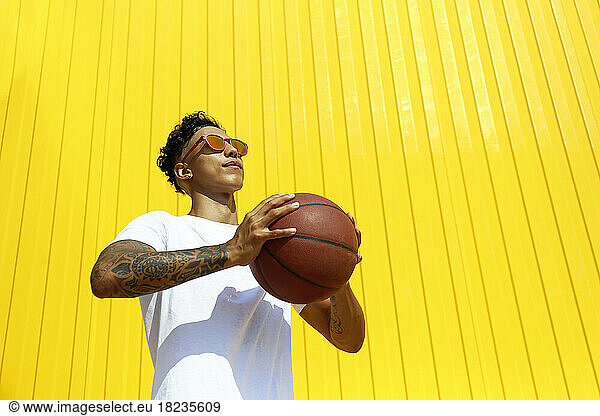 Young man holding basket ball in front of yellow wall