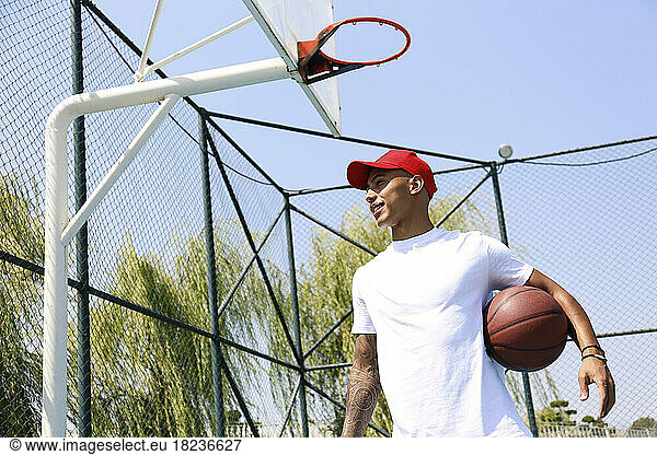 Young man holding basketball under arm on sunny day
