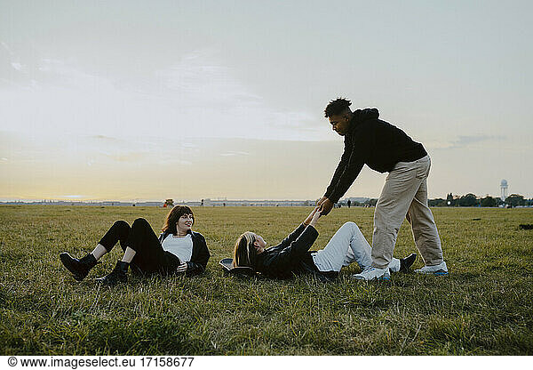 Young man holding hands of female friend lying down on grass in park
