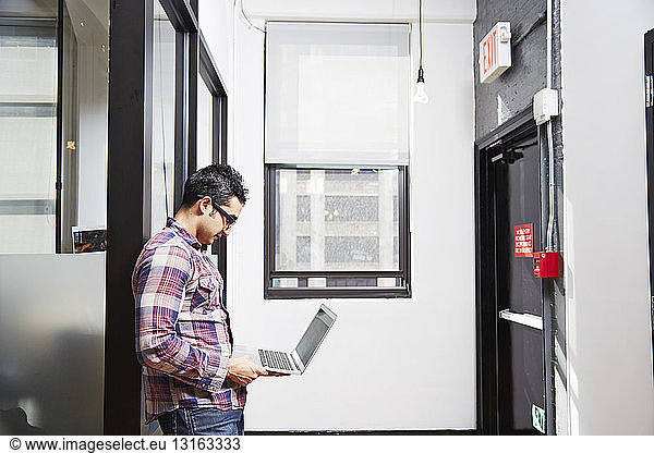 Young man holding laptop in corridor