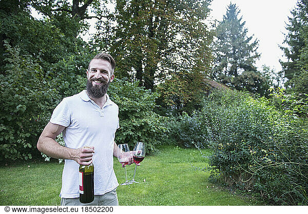 Young man holding red wine with glasses in garden  Bavaria  Germany