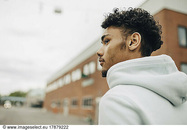 Young man in hooded jacket looking away at street