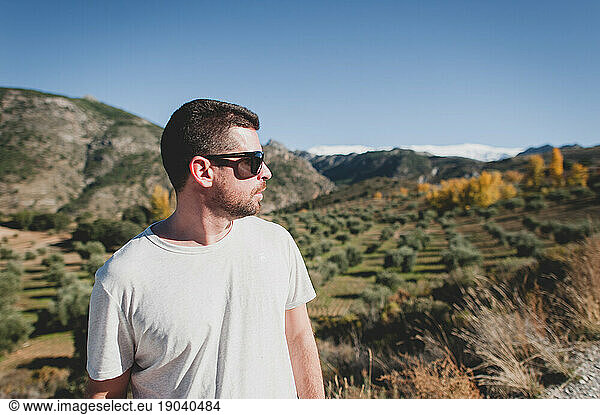 Young man in sunglasses looking at olive trees and snowy mountain