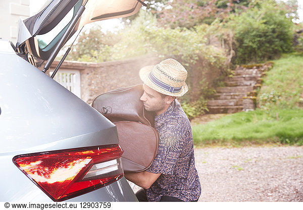 Young man in trilby removing luggage from car boot outside hotel