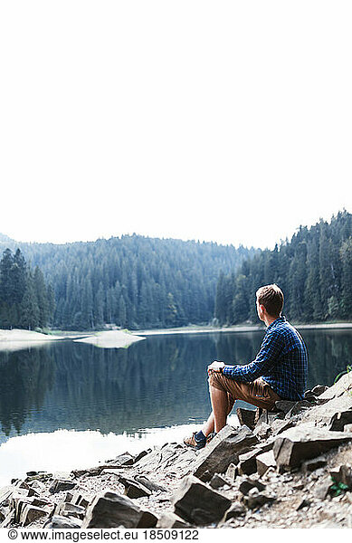 young man is alone near a mountain forest lake