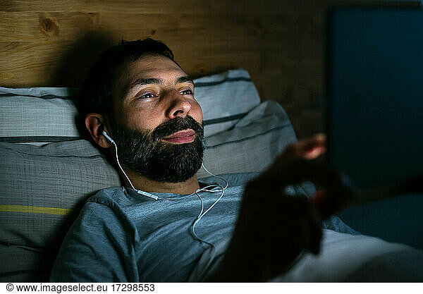 Young man is surfing on Internet using tablet on bed at night