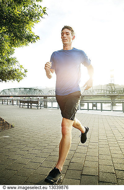 Young man jogging on promenade during sunny day