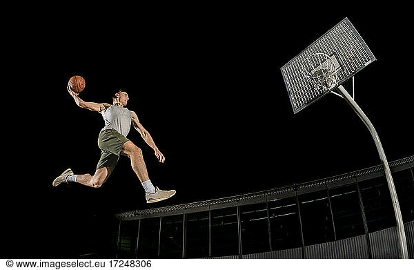 Young man jumping while playing basketball at night
