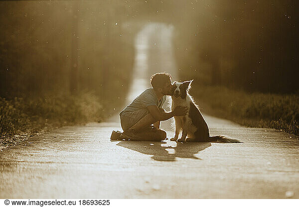 Young man kissing border collie dog on road at sunset