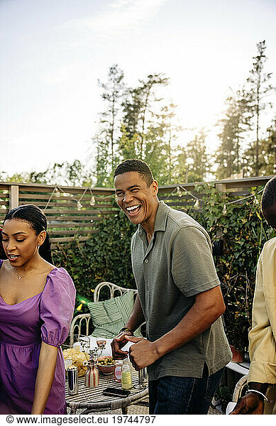 Young man laughing while celebrating with friends at party in back yard