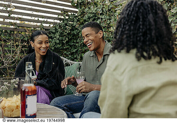 Young man laughing while enjoying drinks with female friends at dinner party