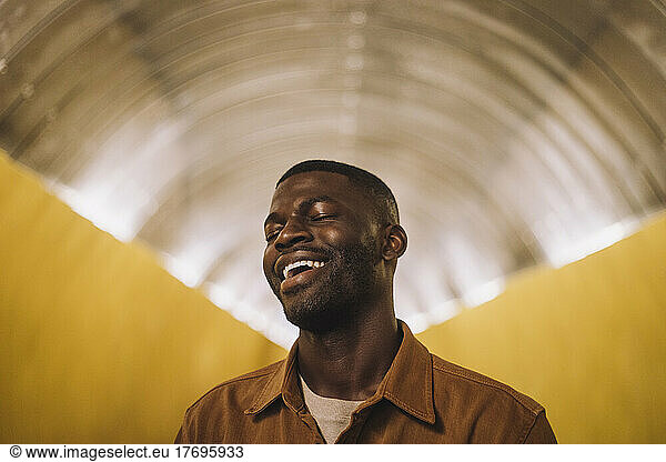 Young man laughing with eyes closed in illuminated tunnel