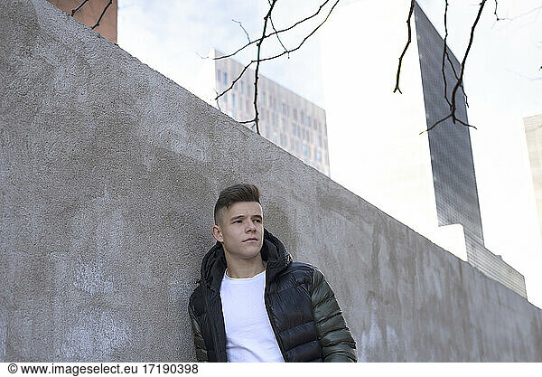 Young man leaning on concrete wall hands on pocket. looking away