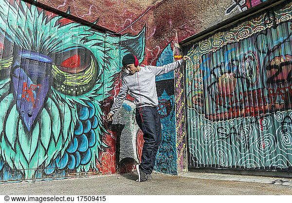 Young man liestening music with headphones dancing in front of graffiti