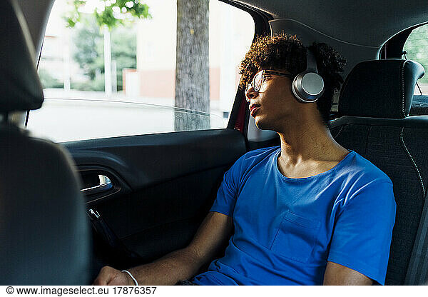 Young man listening music through wireless headphones looking out of car window