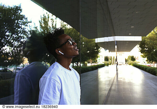Young man listening to music through in-ear headphones leaning on wall
