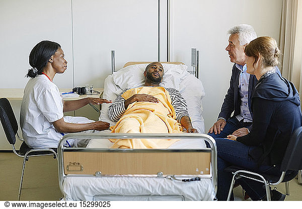 Young man looking at family while doctor discussing in hospital ward