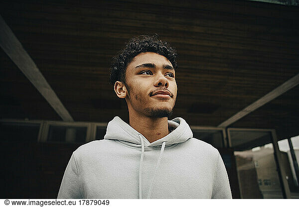 Young man looking away standing under bridge