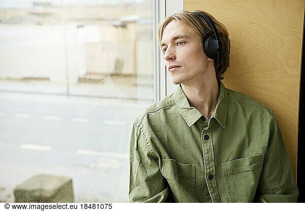 Young man looking out of window wearing bluetooth headphones