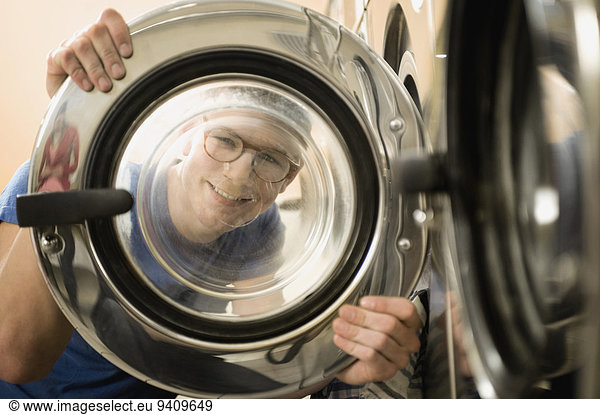 Young man looking through window of washing machine  smiling